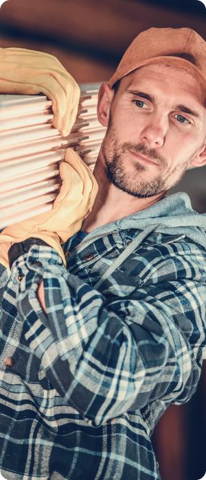 Man wearing gloves and a plaid shirt carrying a stack of wooden planks.